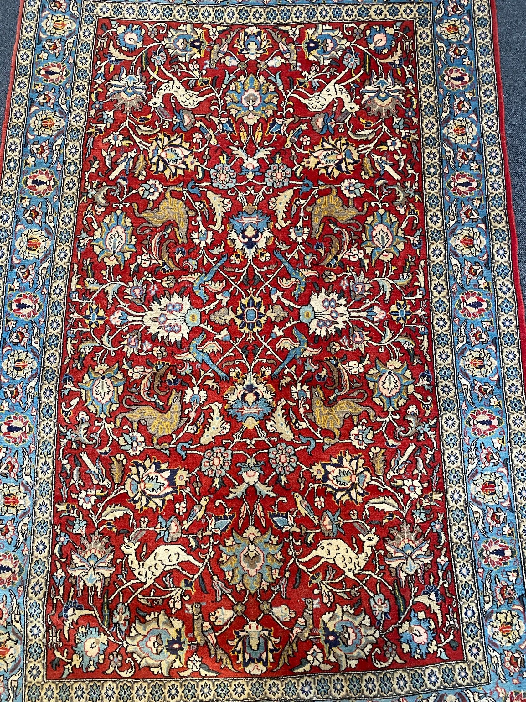 A Persian Qum red ground rug woven with animals and exotic birds among stylised flower heads 220 x 125 cms